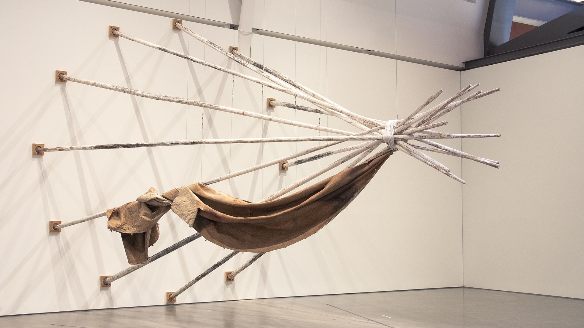 artwork in a gallery: twelve wooden tepee poles painted white, steel cable, charcoal, rope, digital print on linen