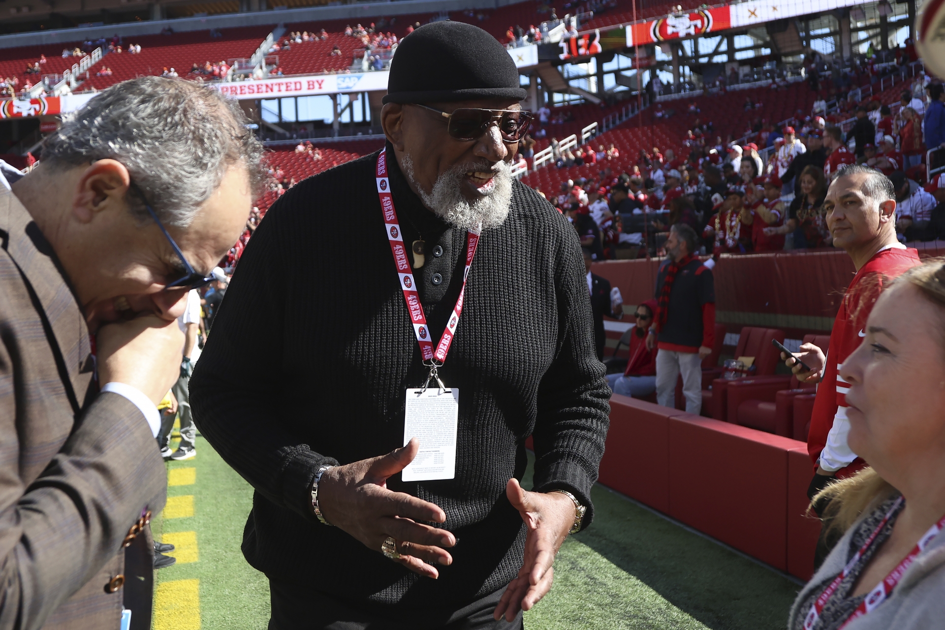 Harry Edwards stands on the sidelines of a football field speaking joyfully to a group of people.