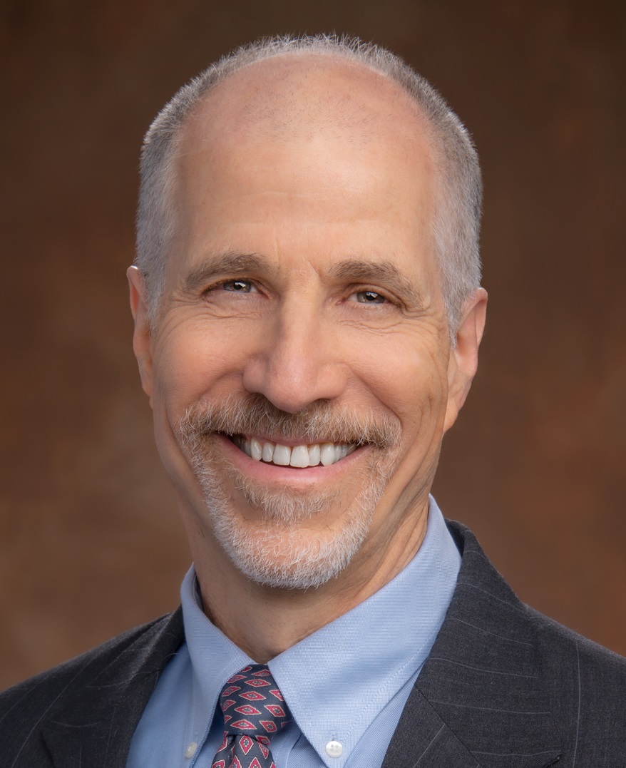 headshot of Severin Borenstein in a jacket and tie, against a chocolate-colored background