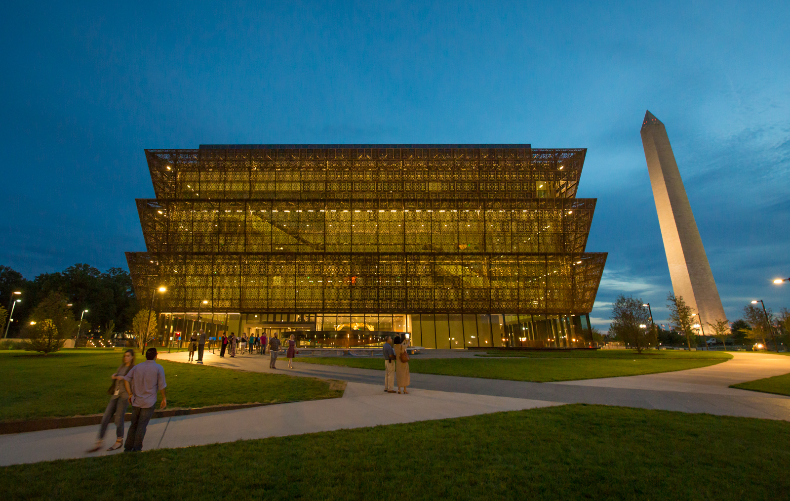 a multistory museum with a brown lattice exterior pictured at night, with a white obelisk rising in the background.