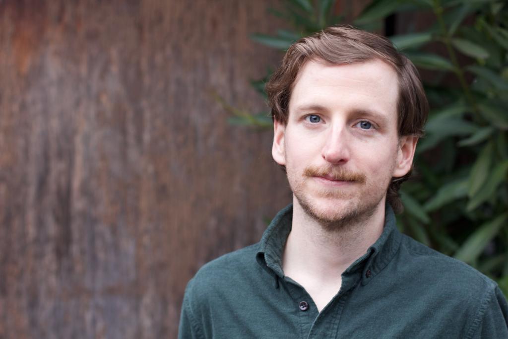 a headshot of a man looking pensive standing in front of a tree