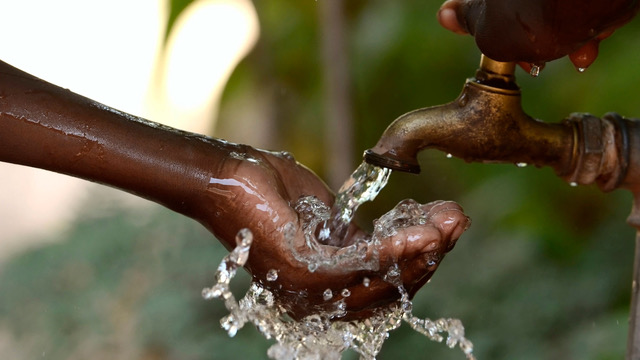 Water pours from an outdoor faucet into a cupped hand.